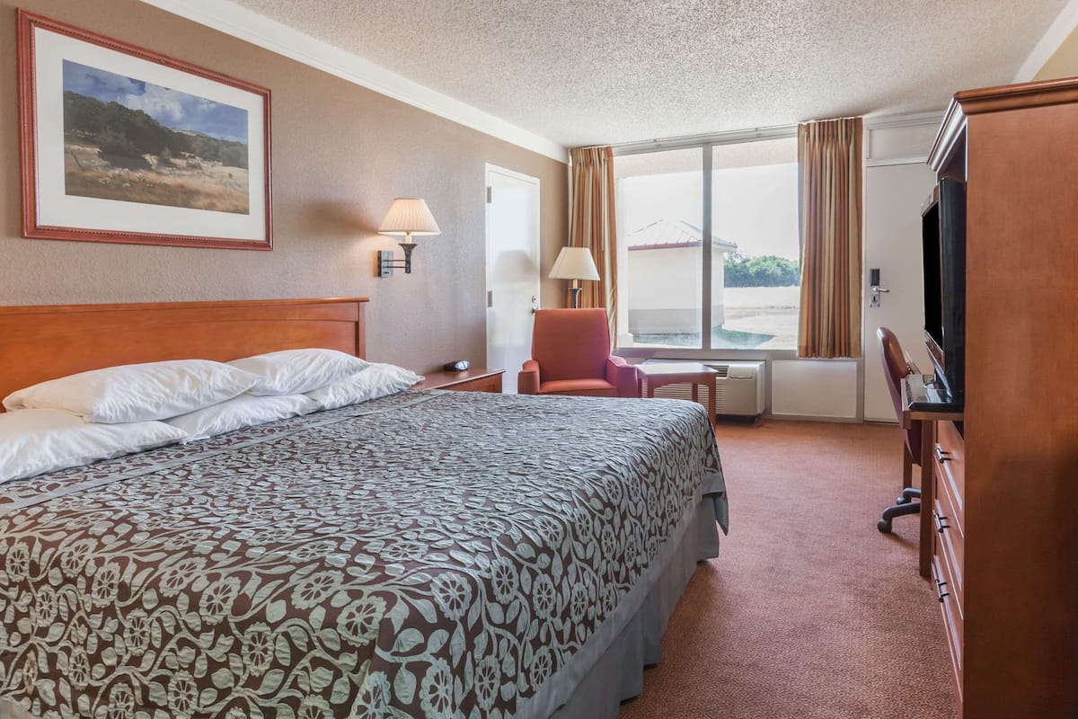 A hotel room with a large bed, a desk, a chair, a television, and a window with curtains.