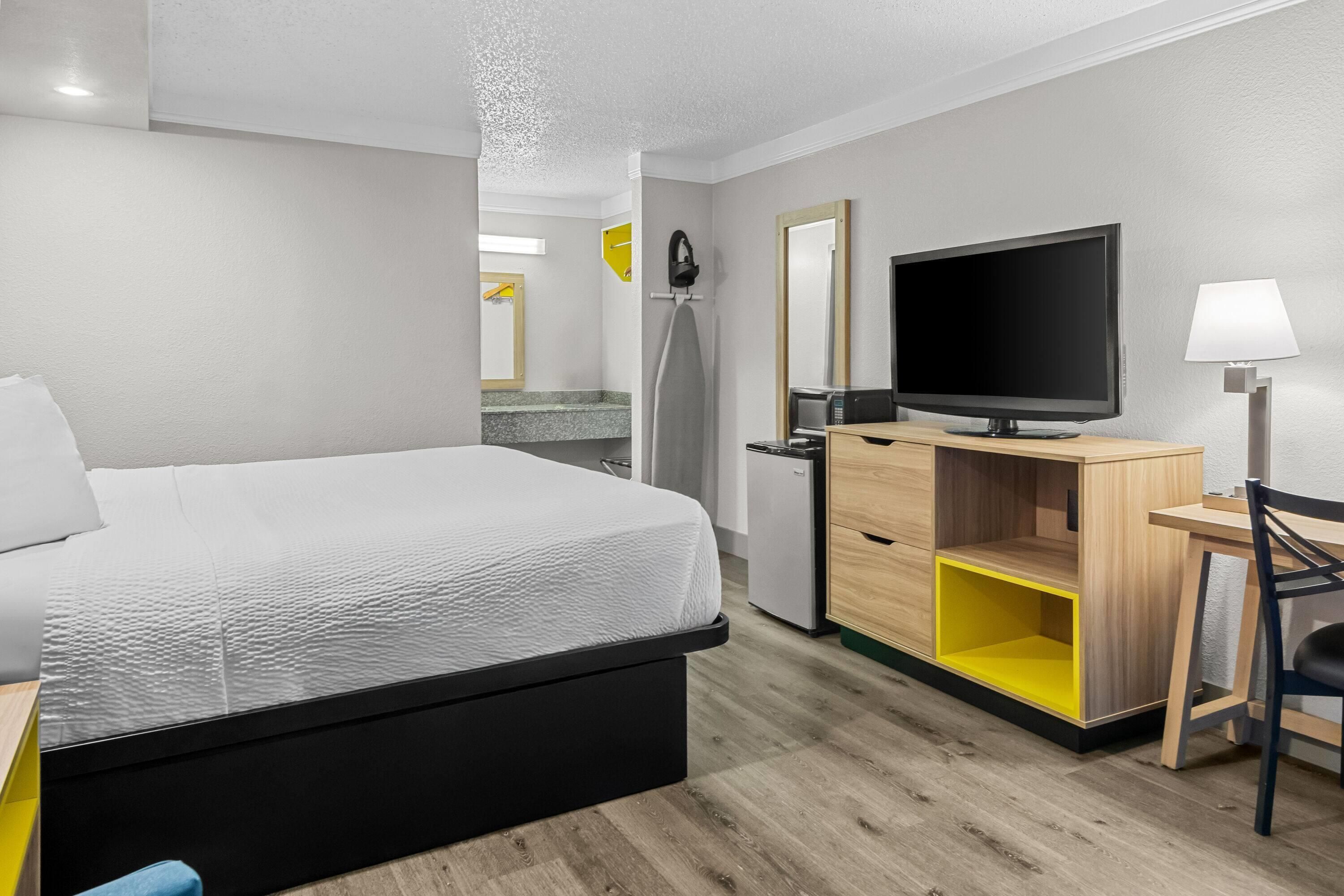 Een moderne hotelkamer met een bed, een televisie, een bureau met een stoel en een spiegel.