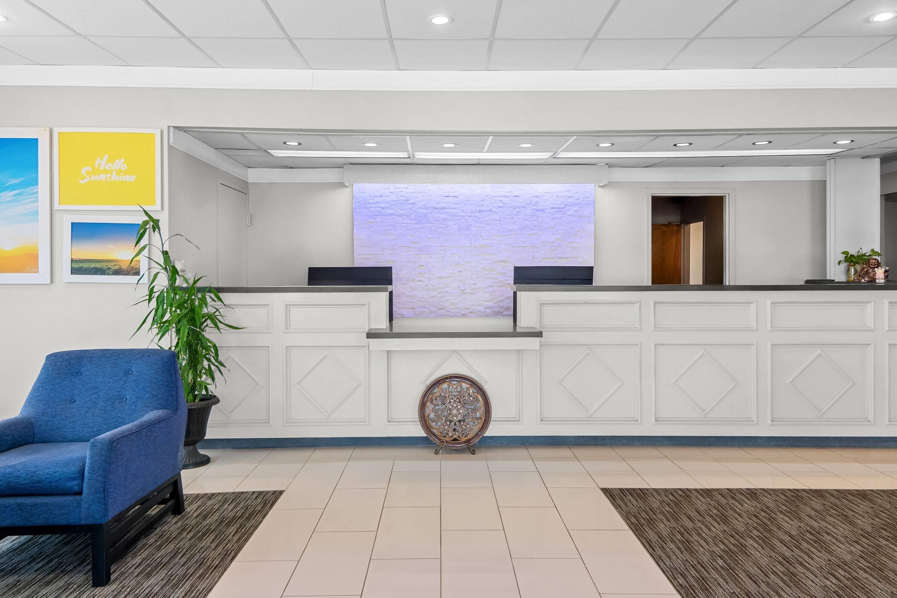 A reception area with a reception desk, a blue chair, a potted plant, and a decorative wall piece.