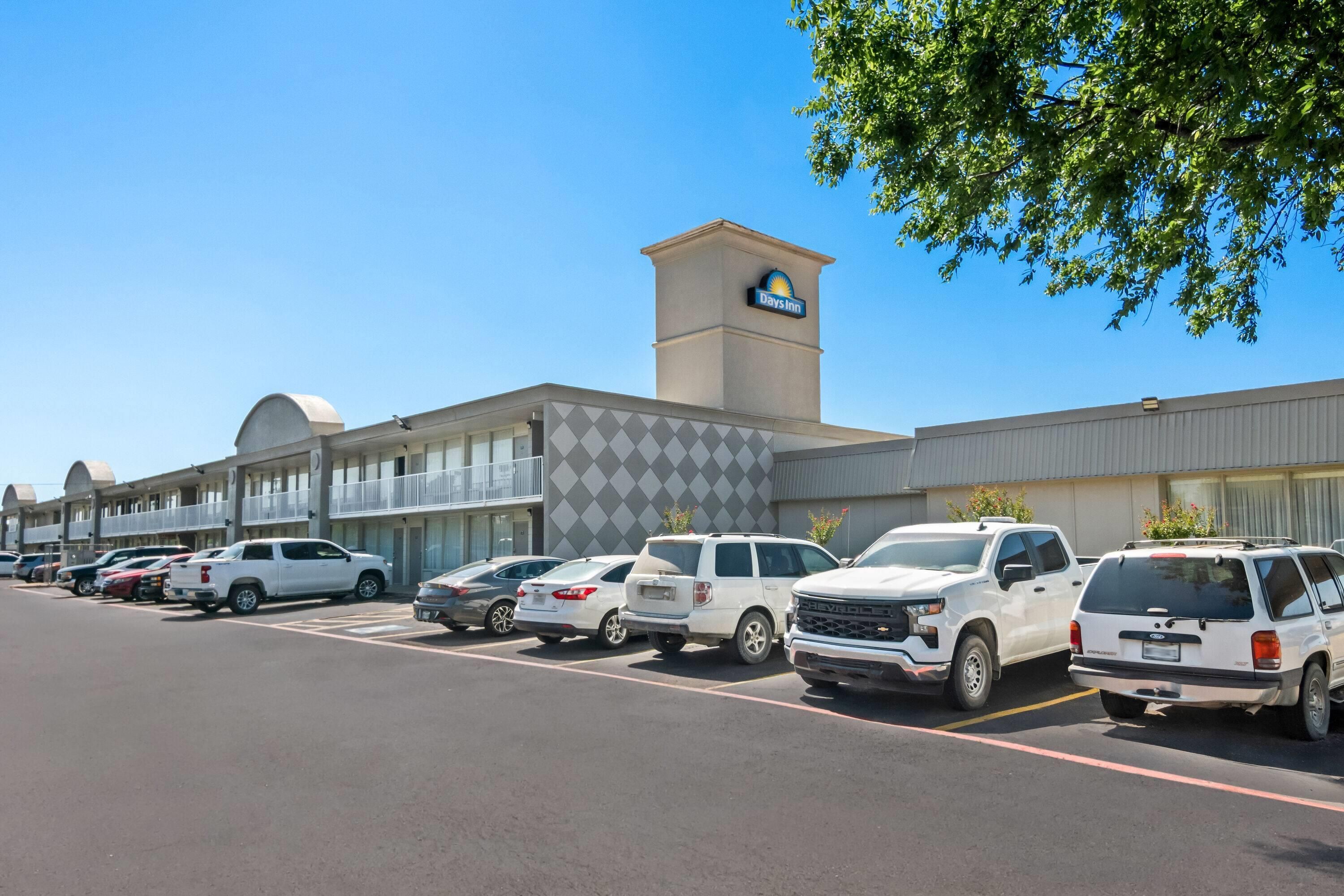 A hotel with a Days Inn sign, a parking lot with several SUVs, and a building with a modern design.