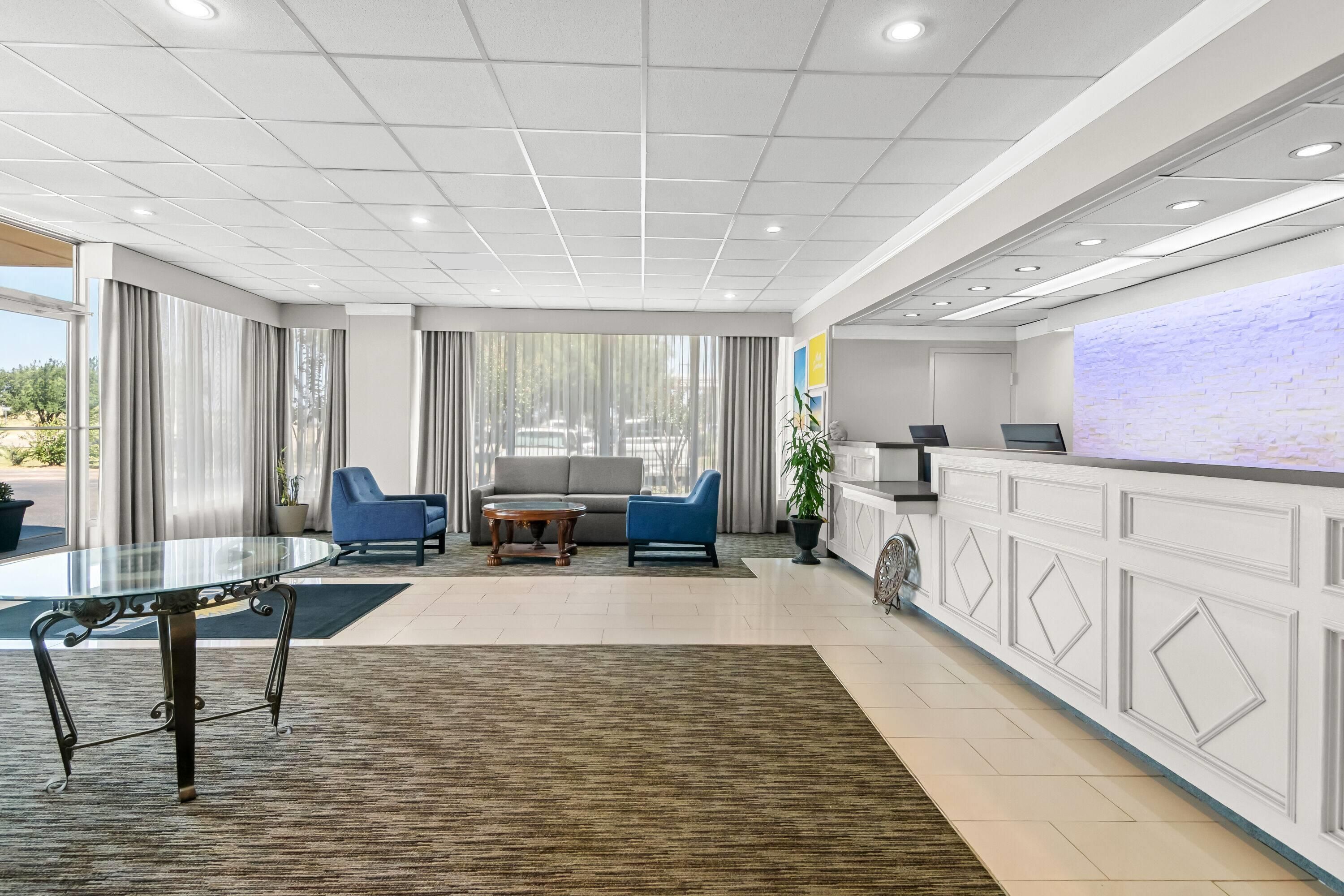A modern hotel lobby with a reception desk, seating area, and a glass coffee table.