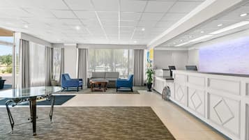 A modern hotel lobby with a reception desk, seating area, and a glass coffee table.