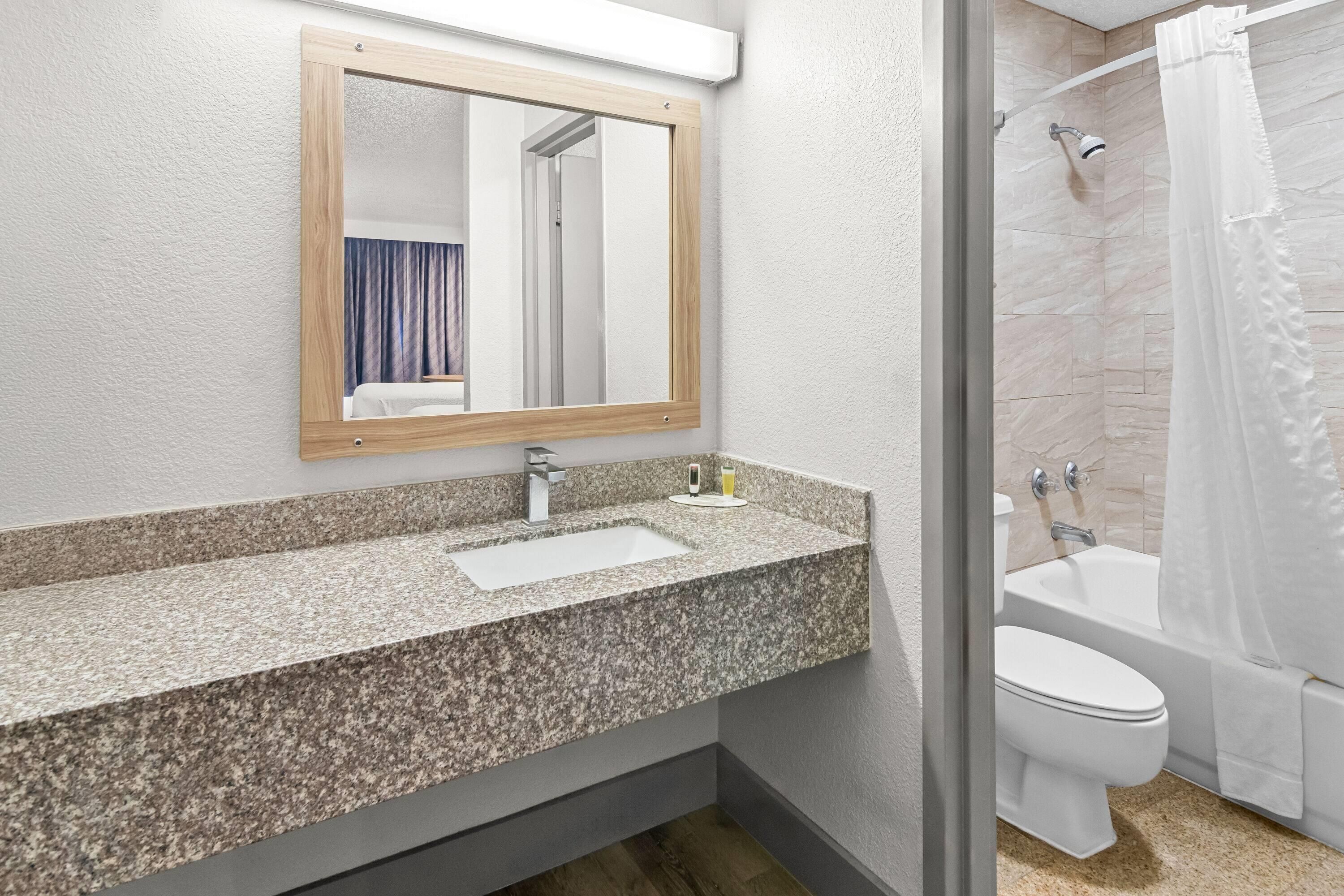 Bany amb taulell de granit, un lavabo, un mirall, un vàter i una zona de dutxa.