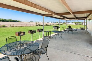 An outdoor patio with a covered area, metal tables and chairs, and a view of a grassy field. - Days Inn by Wyndham Hillsboro TX (Hillsboro)