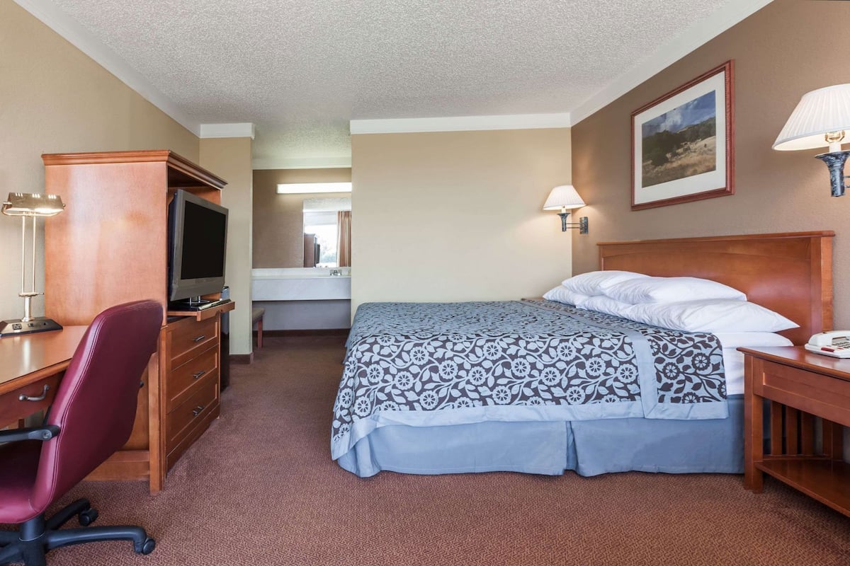 A hotel room with a bed, desk, chair, television, and two wall lamps.
