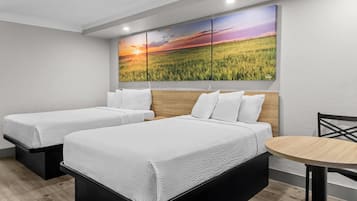 Une chambre d’hôtel avec deux lits, une tête de lit en bois, une table ronde et un grand tableau représentant un paysage accroché au mur.