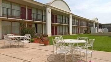 A motel with a row of rooms, outdoor seating, and a lawn.