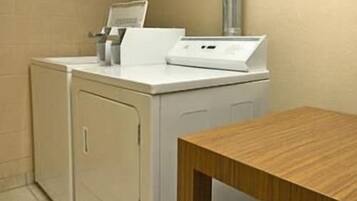 Een wasruimte met een wasmachine en droger, een houten tafel en een betegelde vloer.