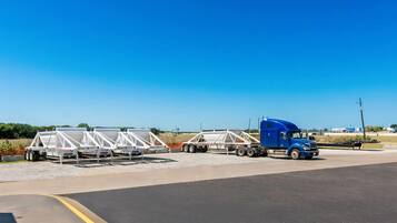 Un camión azul remolqueado estacionado en una carretera, transportando estructuras blancas, posiblemente paneles solares, bajo un cielo despejado.
