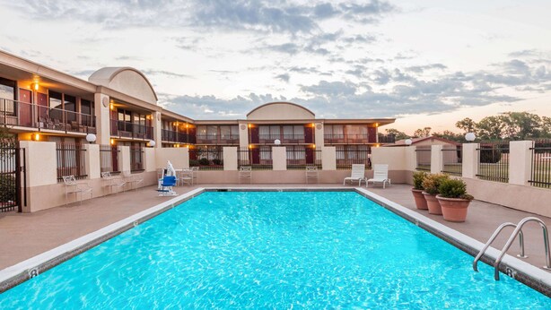 A swimming pool with lounge chairs and a building with balconies. - Days Inn by Wyndham Hillsboro TX (Hillsboro)