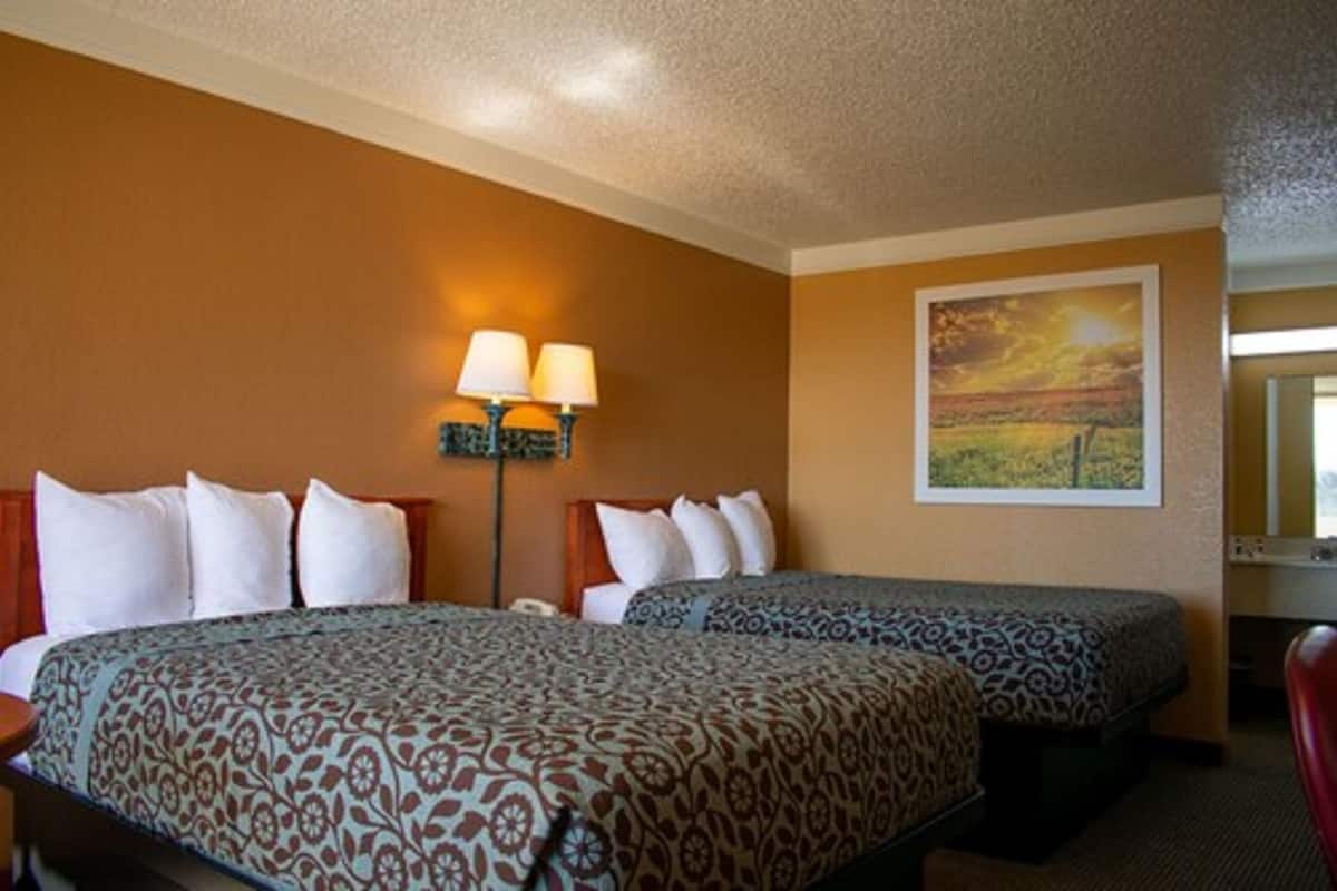 A hotel room with two beds, a nightstand, a lamp, and a painting on the wall.