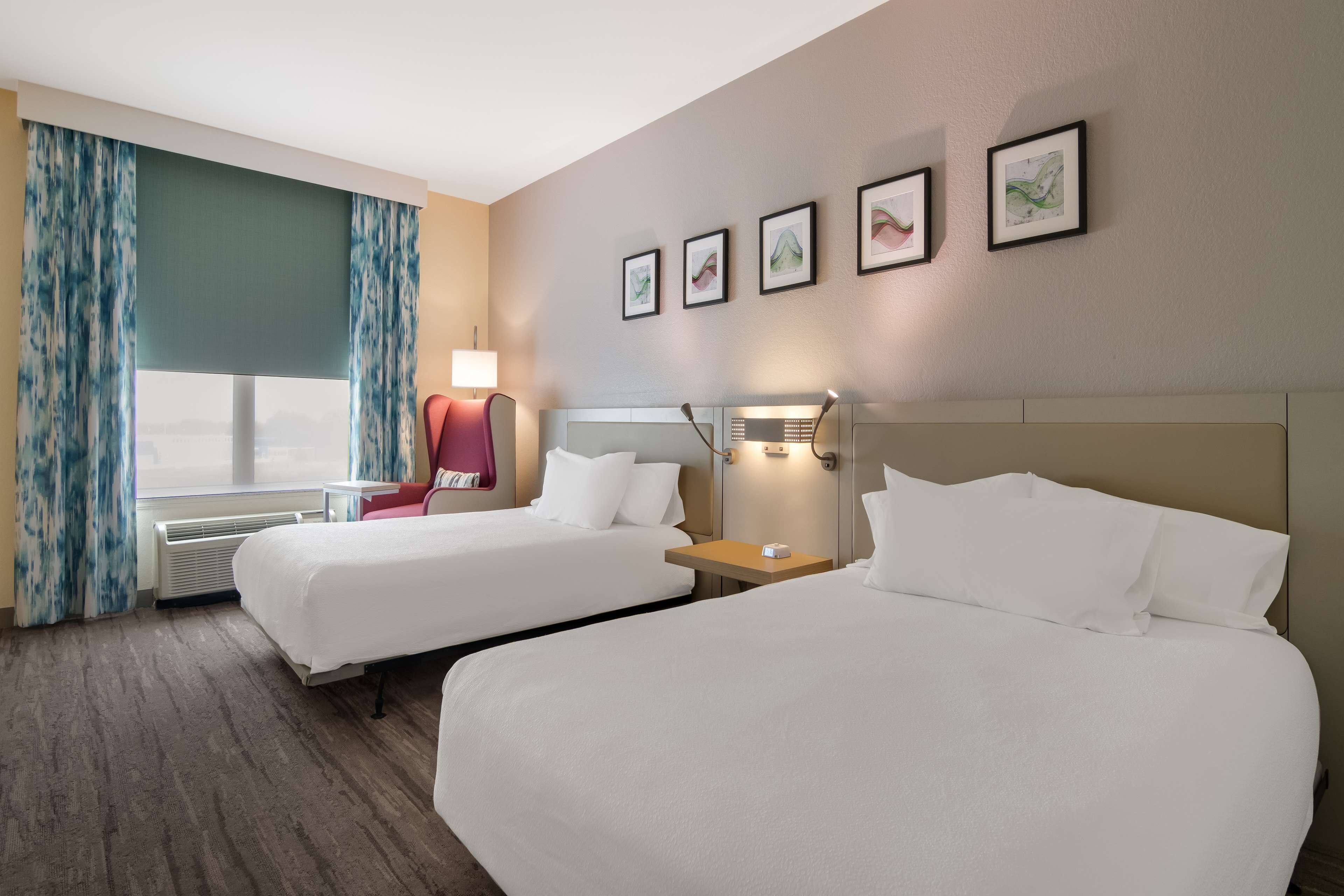 Habitación de hotel con dos camas, un escritorio, una silla y una ventana con cortinas.