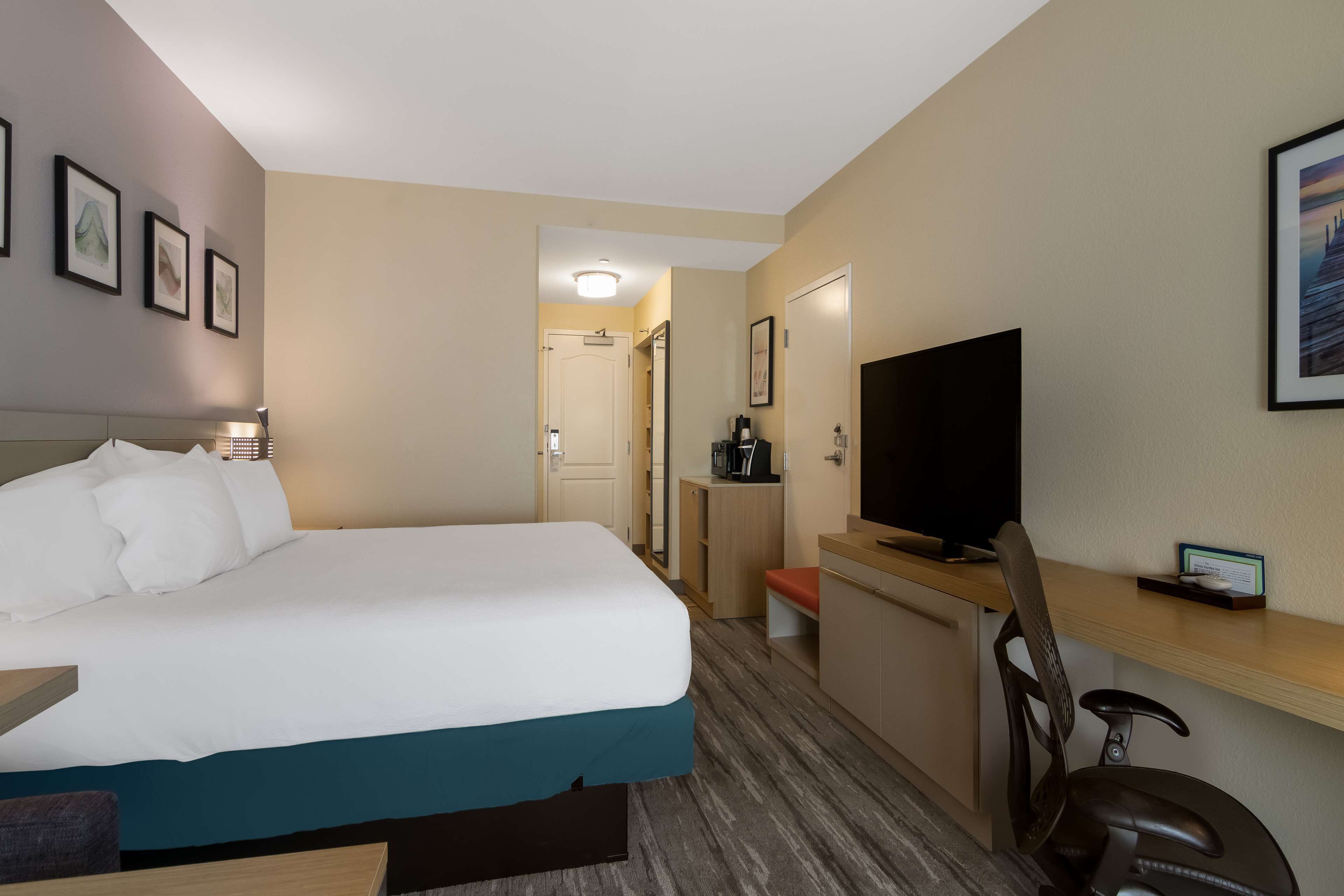 Una habitación de hotel con cama, escritorio, silla, televisor y cafetera.
