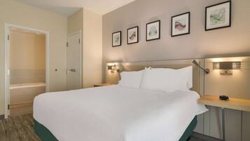 Una habitación de hotel con una cama grande, una mesita de noche, una lámpara de pared y una puerta que da al baño.