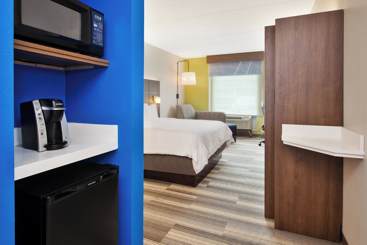 A hotel room with a bed, a coffee maker, a microwave, and a small refrigerator.