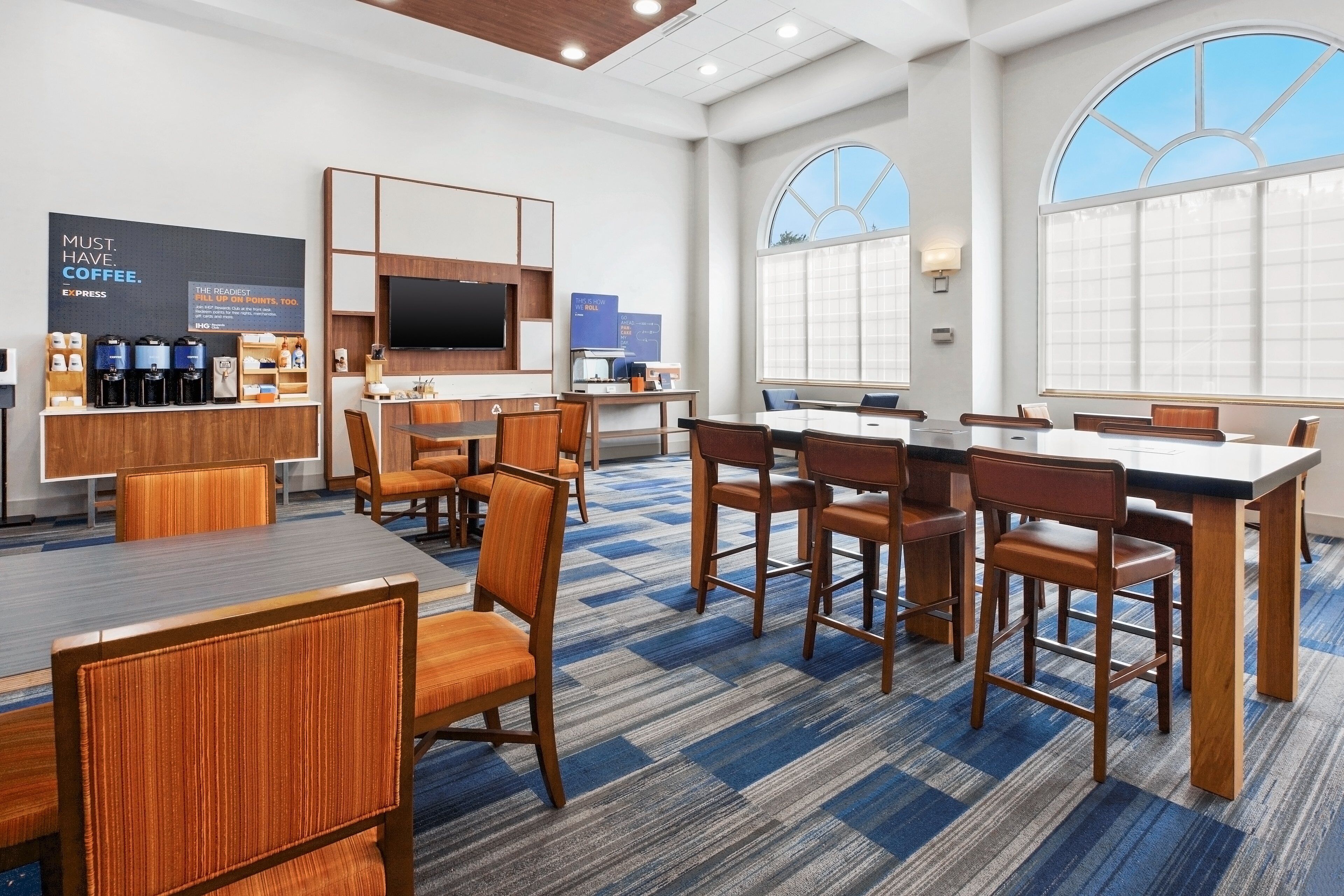 A modern hotel lobby with a coffee station, seating area, and large windows.