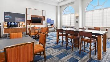 A modern hotel lobby with a coffee station, seating area, and large windows.