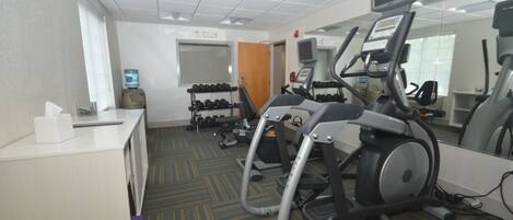 A gym with treadmills, dumbbells, and a desk with a tissue box.