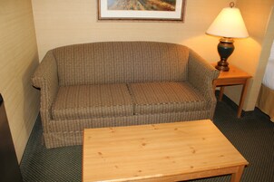Una habitación con un sofá marrón, una mesa de centro de madera y una lámpara en una mesita auxiliar.