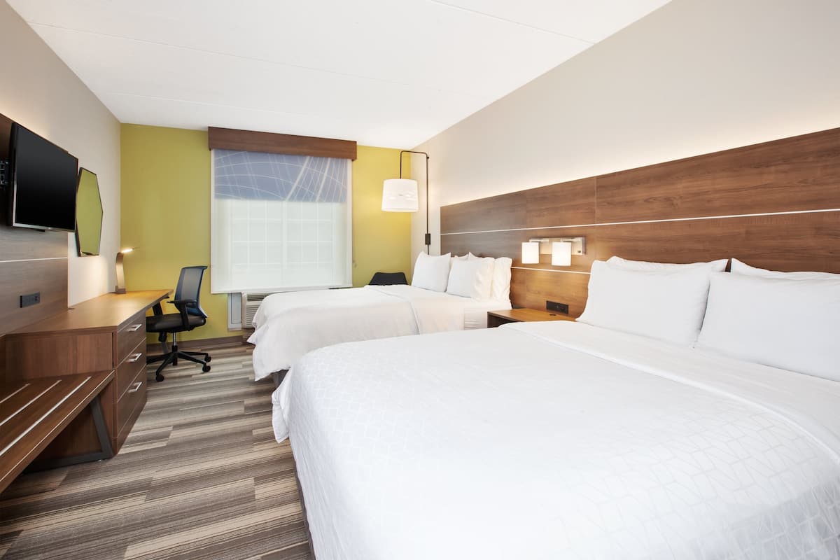A hotel room with two beds, a desk, a chair, a TV, and a window with curtains.