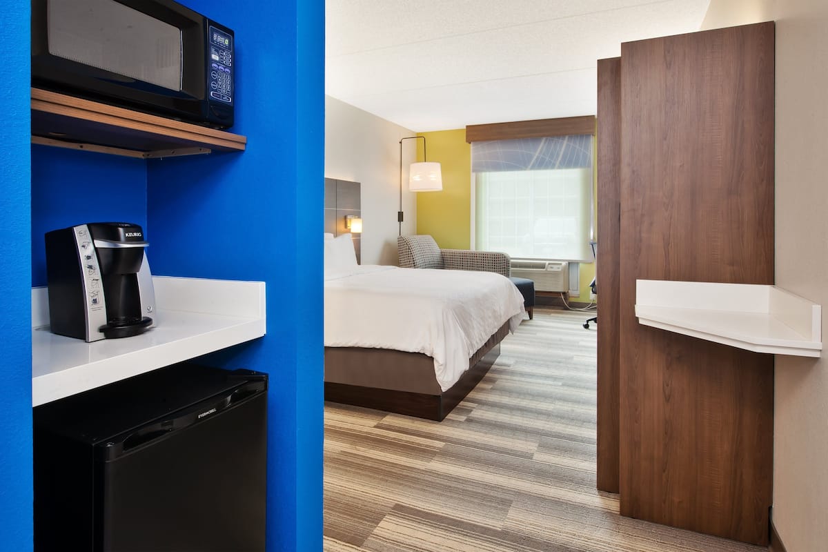 A hotel room with a bed, a coffee maker, a microwave, and a small refrigerator.