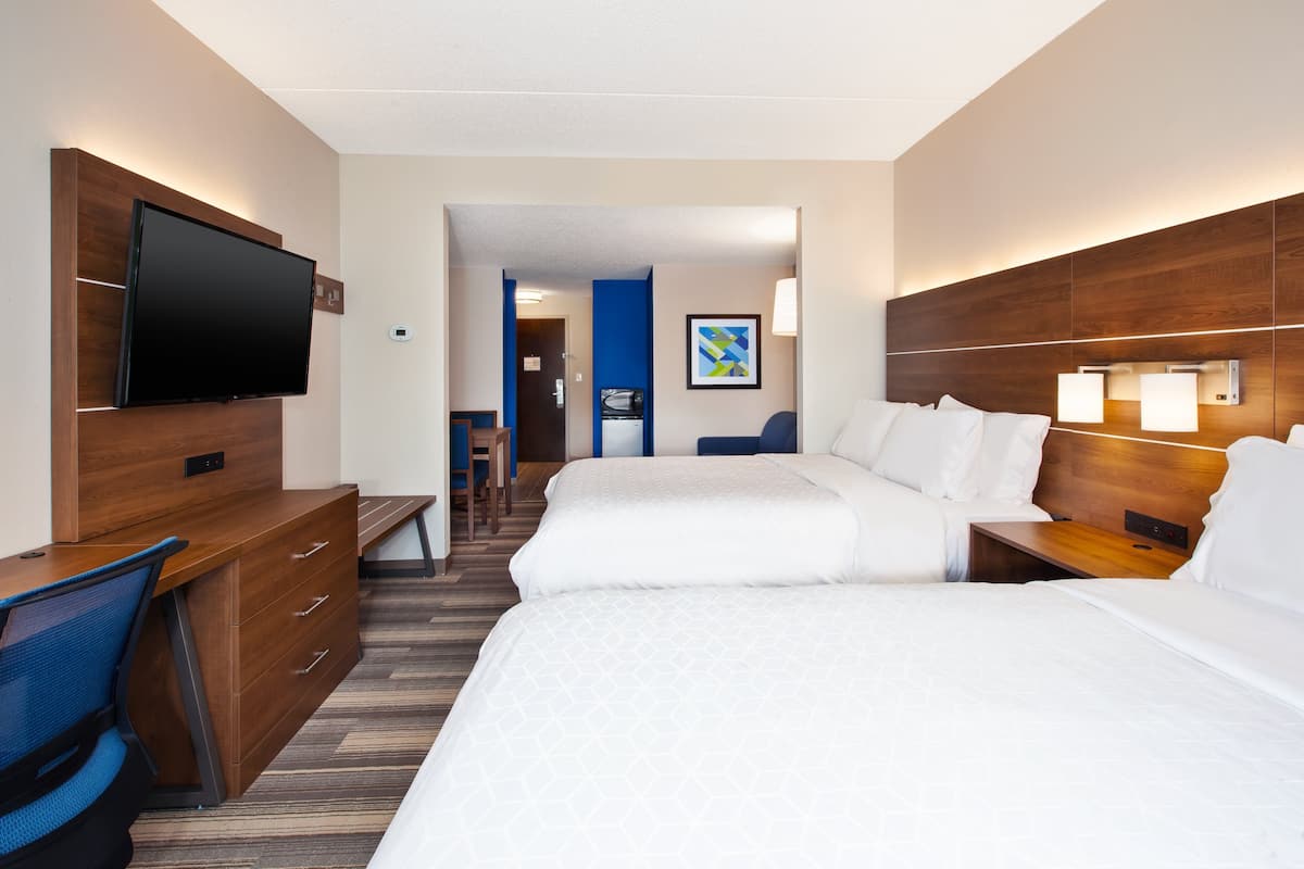 A hotel room with two beds, a desk with a chair, a flat-screen TV, and a bathroom visible through an open door.
