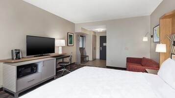 Habitación de hotel con cama, escritorio con televisor de pantalla plana, cafetera, microondas, silla y sofá rojo.