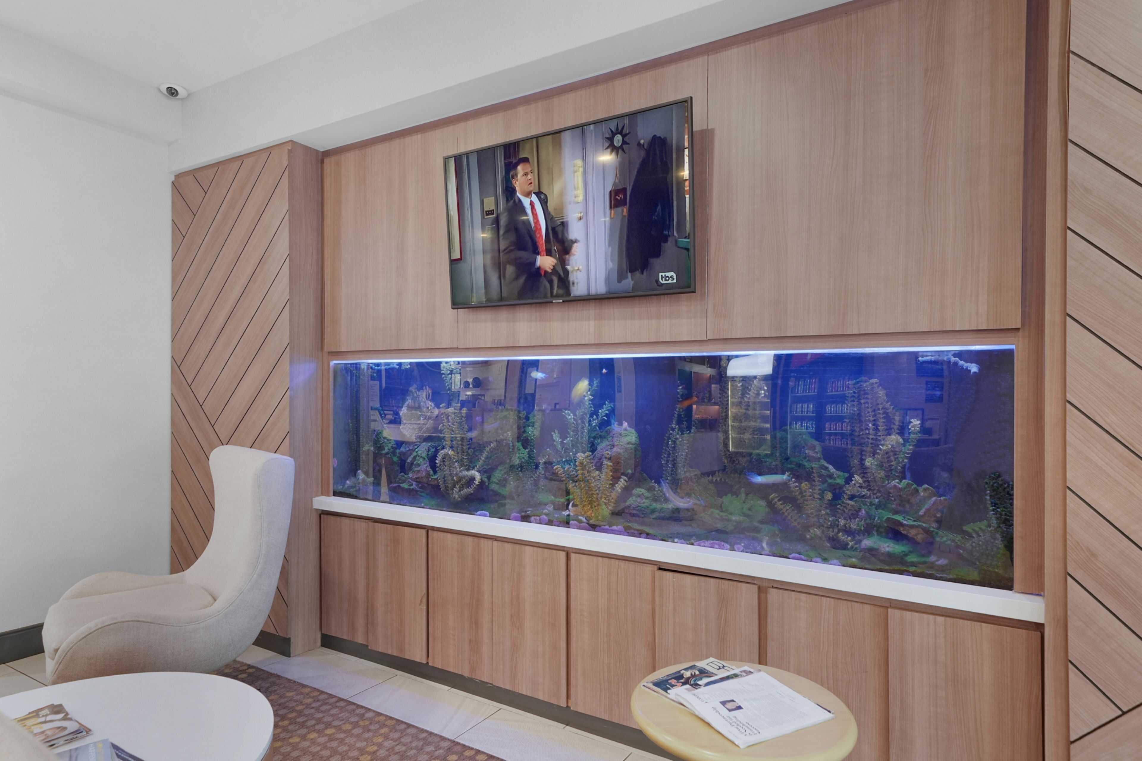 Un vestíbulo moderno con un gran acuario, un área de estar acogedora y un televisor montado.