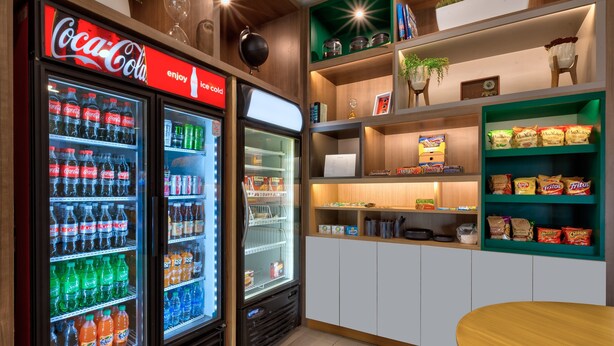 Un refrigerador de Coca-Cola lleno de diversas bebidas, un microondas y estantes con aperitivos y condimentos.