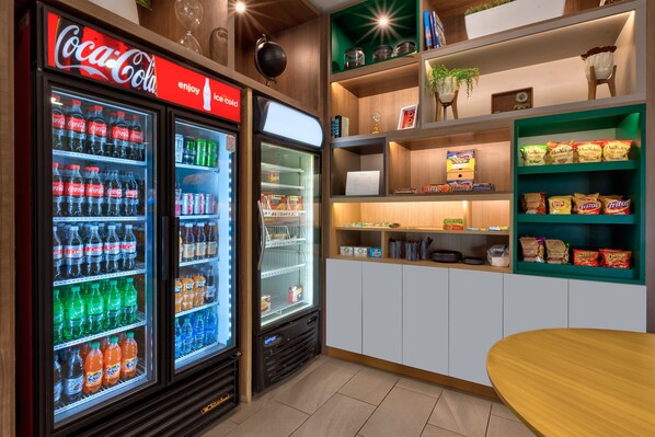 Un frigorifero Coca-Cola pieno di diverse bevande, un forno a microonde e scaffali con snack e condimenti.