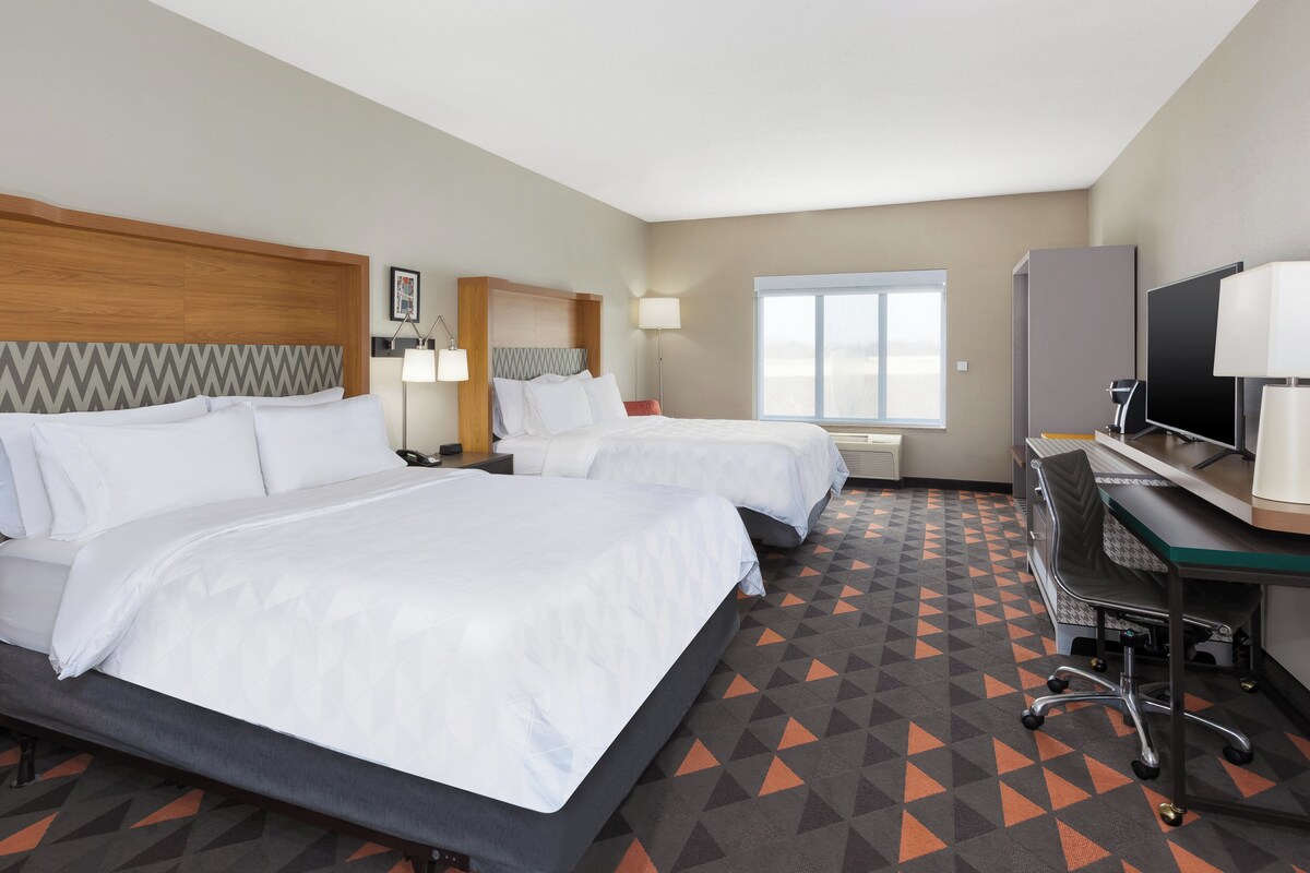 A hotel room with two beds, a desk, a TV, and a large window.