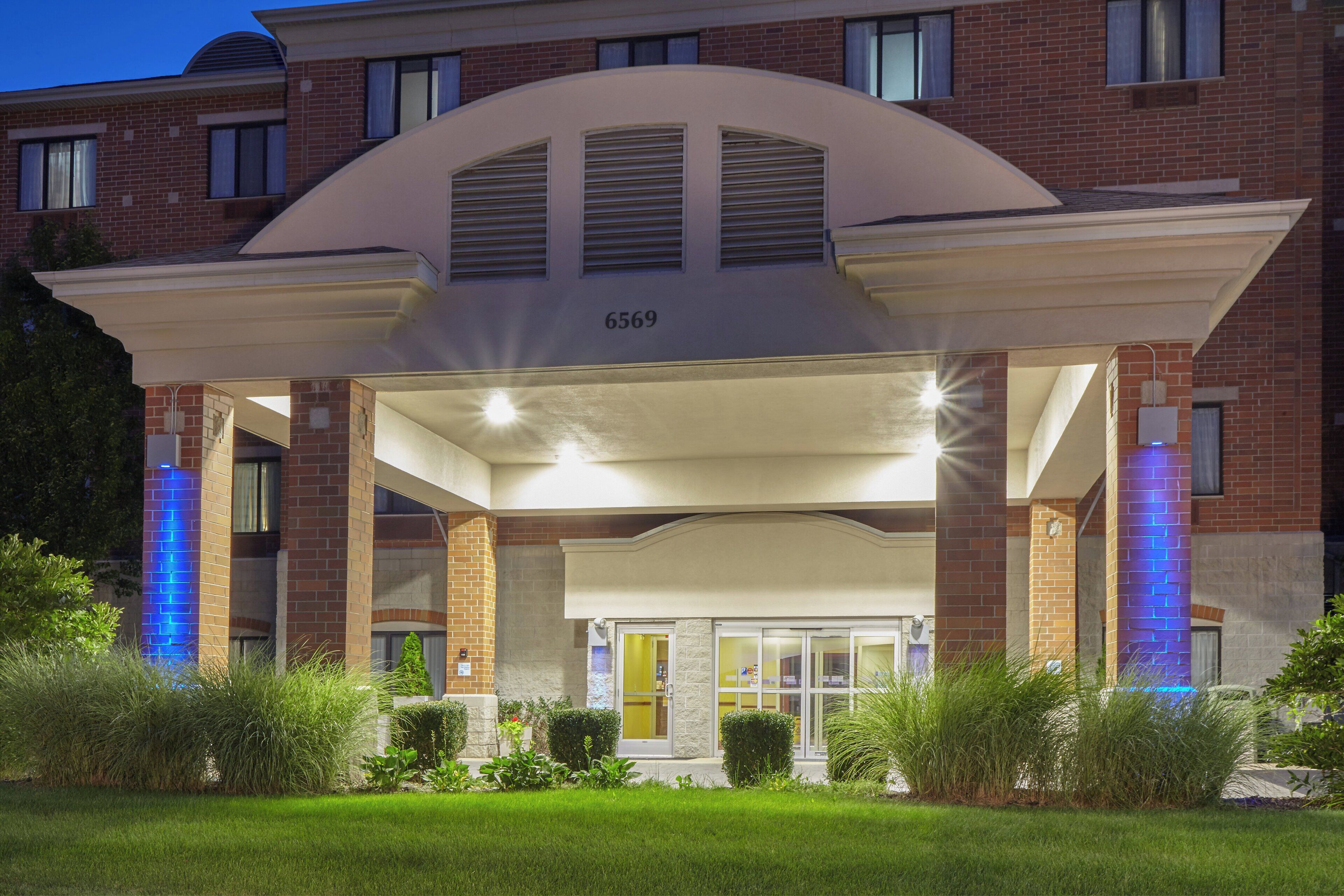 A hotel entrance with a covered porch, brick facade, and illuminated blue accents.