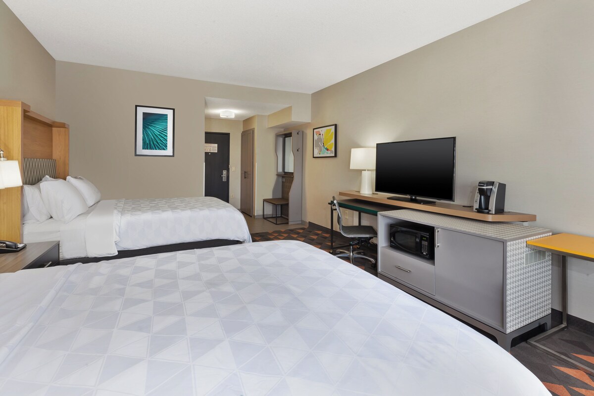 A hotel room with two beds, a desk with a flat-screen TV, a microwave, and a coffee maker.