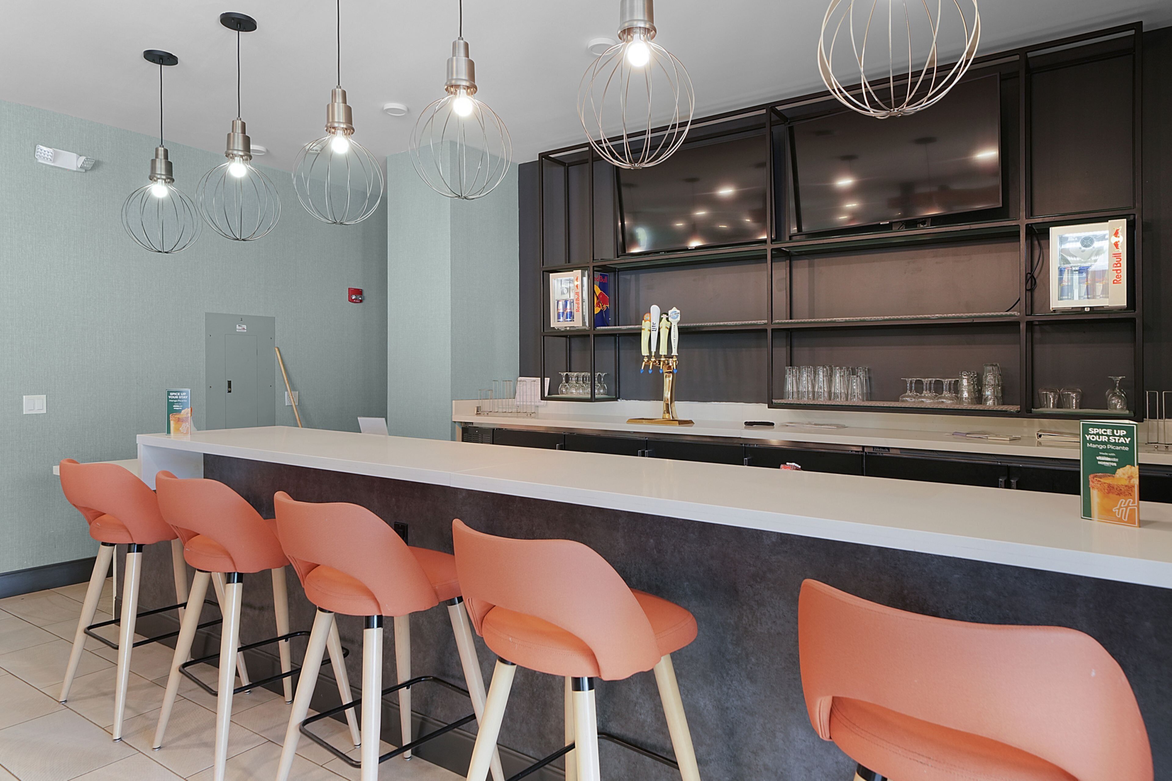 A modern bar area with a counter, bar stools, and overhead lighting.