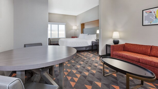 A hotel room with a bed, a round dining table, a sofa, and a small table. - Holiday Inn Grand Rapids - South by IHG (Grand Rapids)