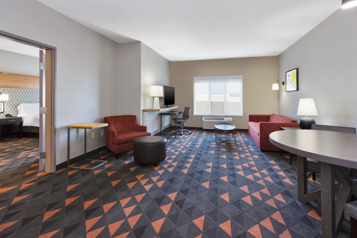 A hotel room with a geometric patterned carpet, a red sofa, a round table, and a TV on a stand.