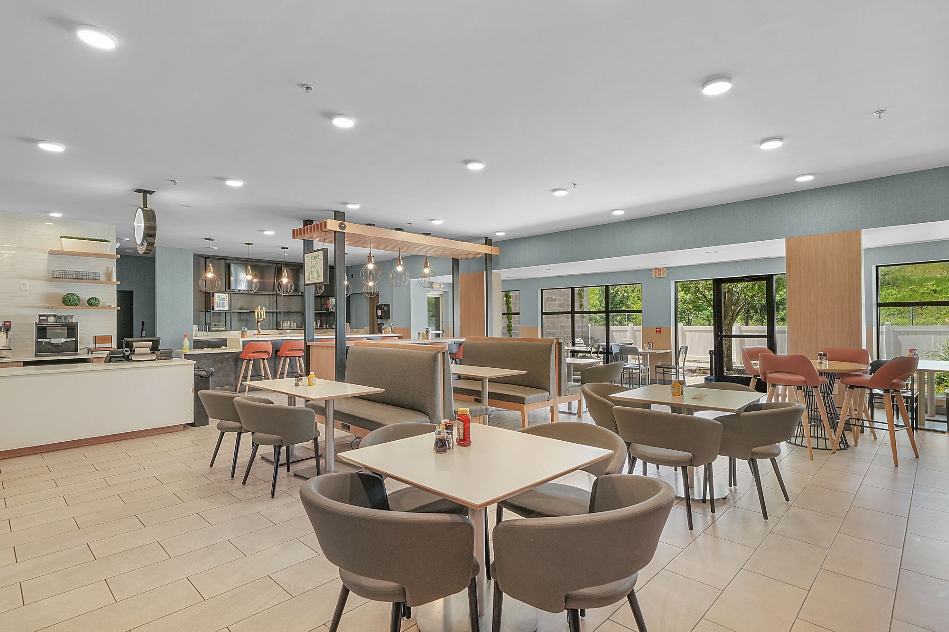 A modern restaurant with multiple seating areas, including tables and booths, and a bar area with a counter.