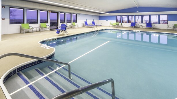 A swimming pool with blue and green lounge chairs, a tiled deck, and large windows. - Holiday Inn Express Rochelle by IHG (Rochelle)