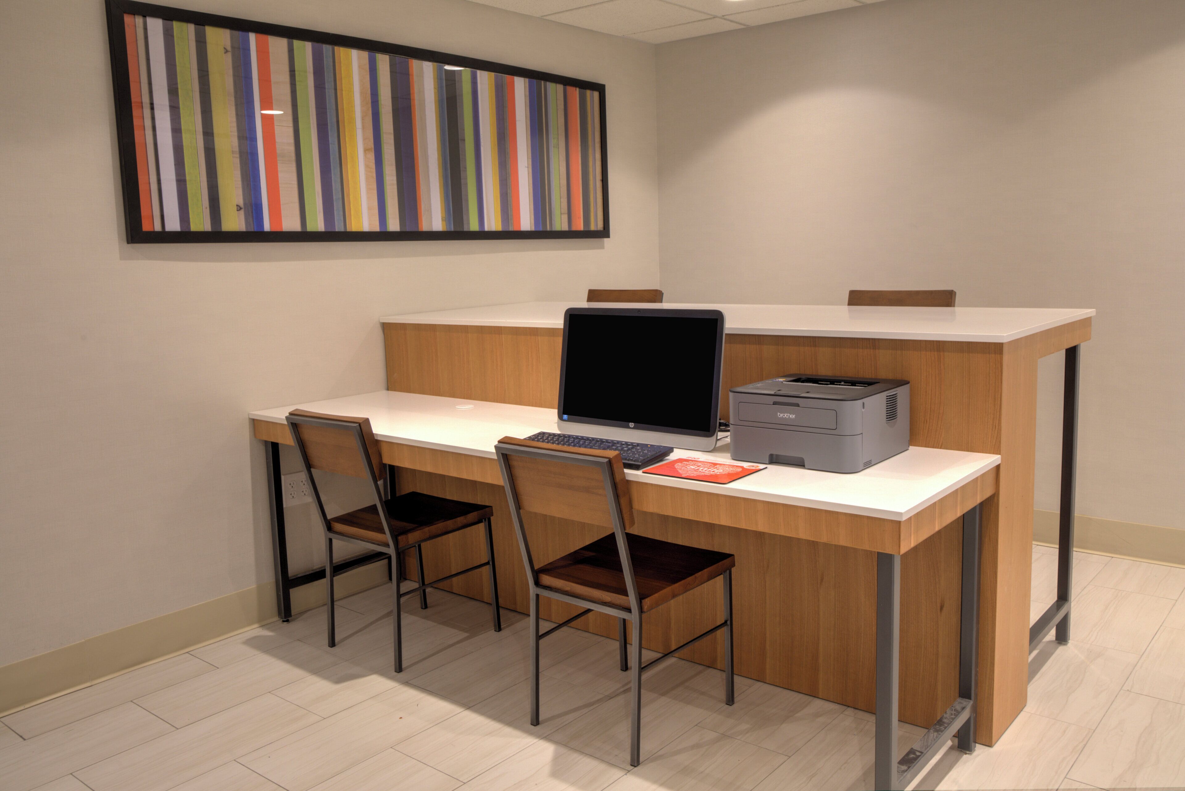 A modern office space with a desk, two chairs, a laptop, a printer, and a colorful abstract painting on the wall.