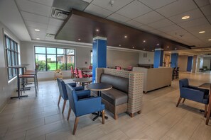 A spacious indoor area with multiple seating options including tables, chairs, and a sofa. There are large windows providing natural light and a view of the outdoors. - Holiday Inn Express Rochelle by IHG (Rochelle)