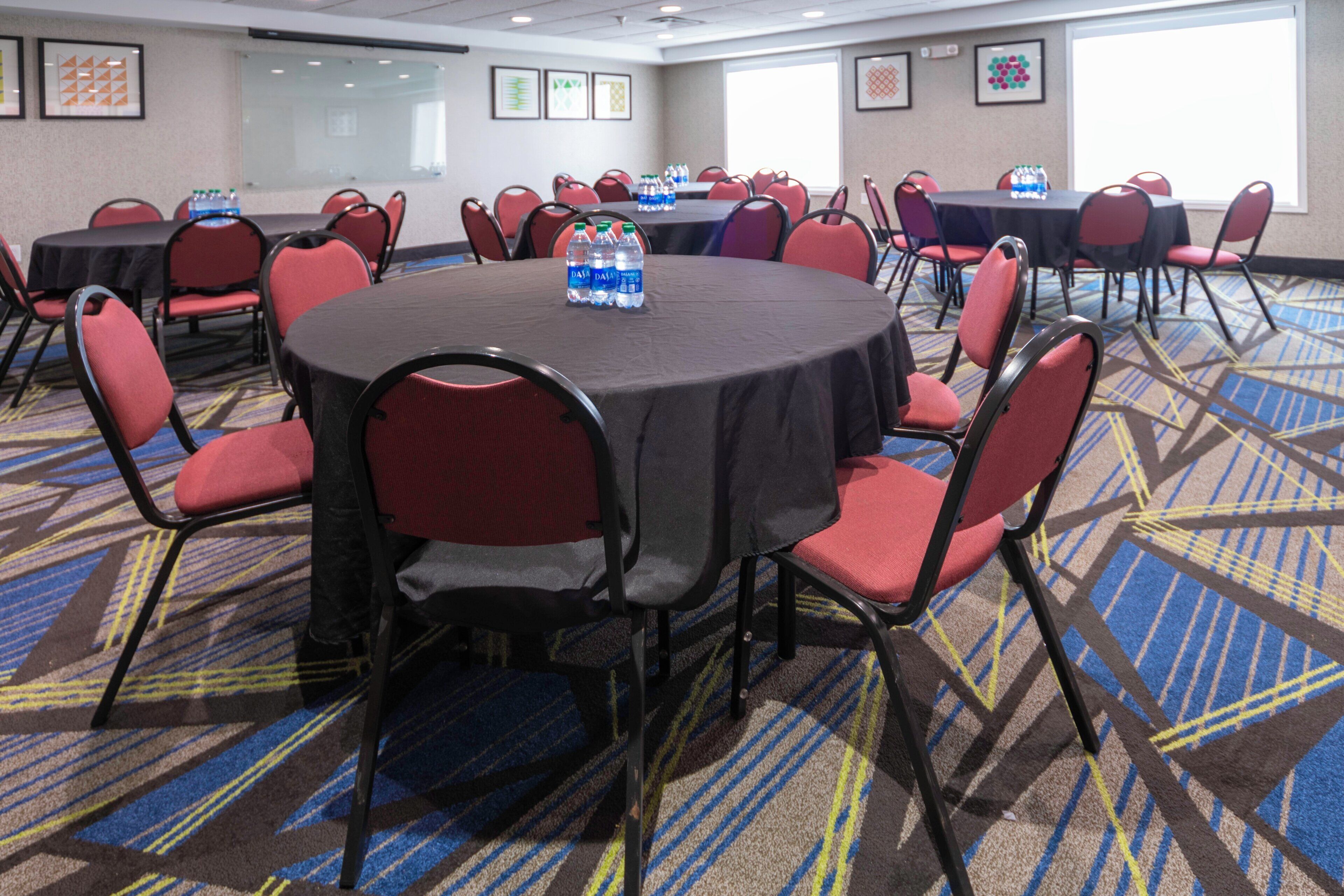 A conference room with round tables and red chairs, equipped with water bottles.