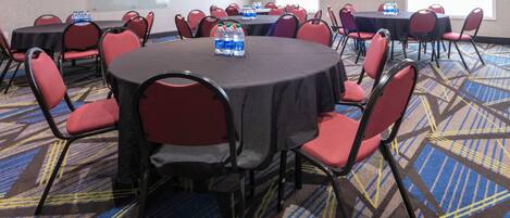 A conference room with round tables and red chairs, equipped with water bottles.