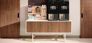 Een koffiehoek met twee koffiemachines, een koffiemolen en diverse koffiepads en verpakkingen.