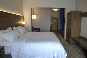 Een hotelkamer met een groot bed, een bureau, een stoel, een garderobe en een badkamer die door een geopende deur zichtbaar is.