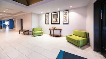 Un hall d’hôtel avec un comptoir d’accueil, deux fauteuils verts, une petite table sur laquelle se trouve un bol, et des œuvres d’art encadrées accrochées au mur.