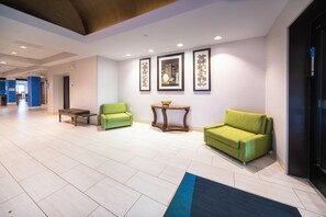 A hotel lobby with a reception desk, two green armchairs, a small table with a bowl, and framed artwork on the wall. - Holiday Inn Express Rochelle by IHG (Rochelle)