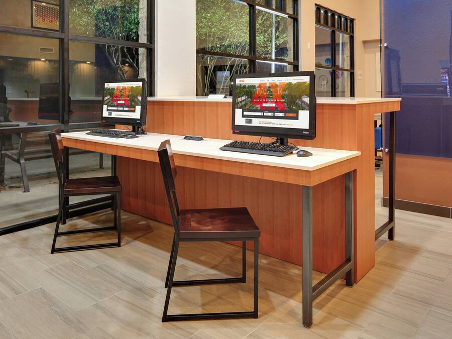 Una recepción con dos monitores de computadora, un mostrador de madera y una sola silla.