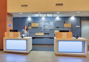 A hotel reception desk with a digital display, a receptionist, and a sign for Holiday Inn Express & Suites. - Holiday Inn Express & Suites Austin Round Rock by IHG (Round Rock)
