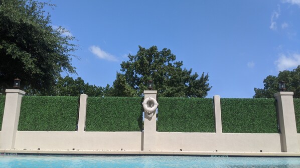 Piscina com parede de sebe verde e dois postes de luz.