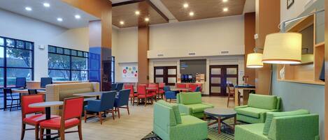 A spacious lobby with multiple seating areas, including sofas and chairs, a coffee station, and a reception desk.